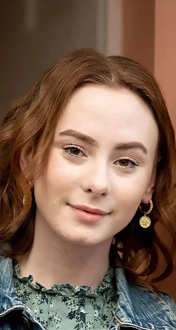 A teenage girl with red hair looking straight at the camera with slight smile