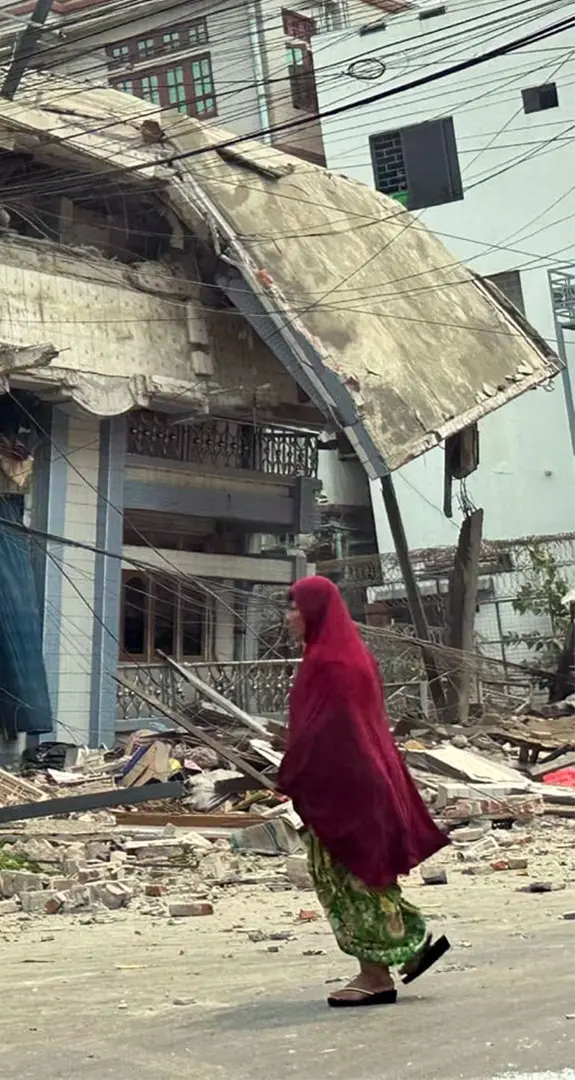 Badly damaged building in the aftermath of the devastating earthquake in Myanmar with woman walking past.