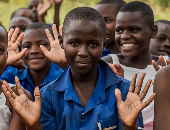 A group of African school children smiling and waving at the camera