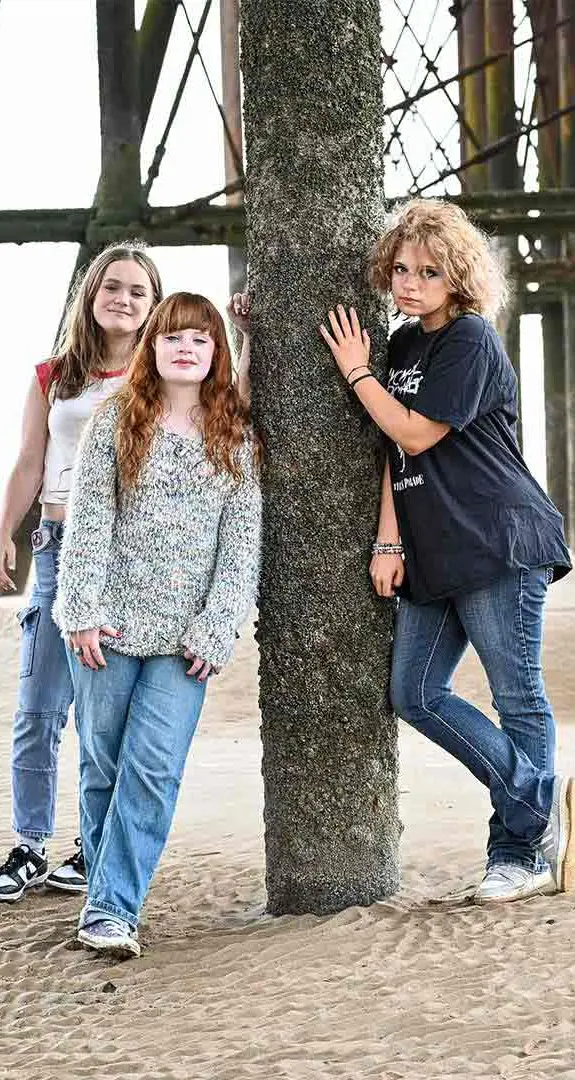 Three teenage girls stand on a beach in Blackpool.