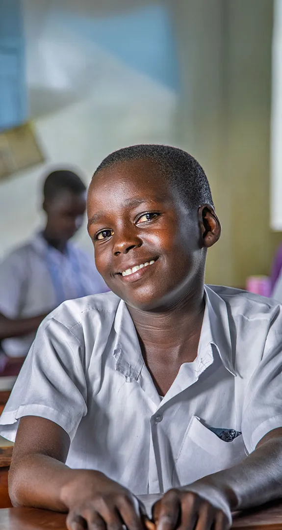 Melisa sitting at school desk smiling at camera with other students out of focus in background