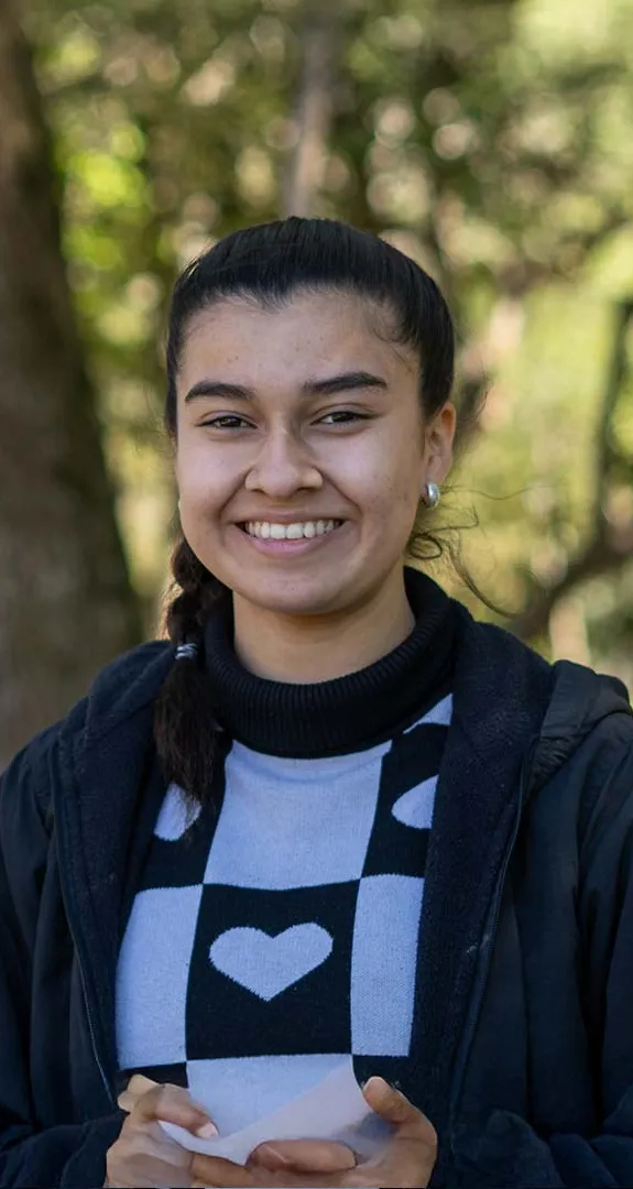 Rebecca standing outside smiling at camera with out of focus trees behind her