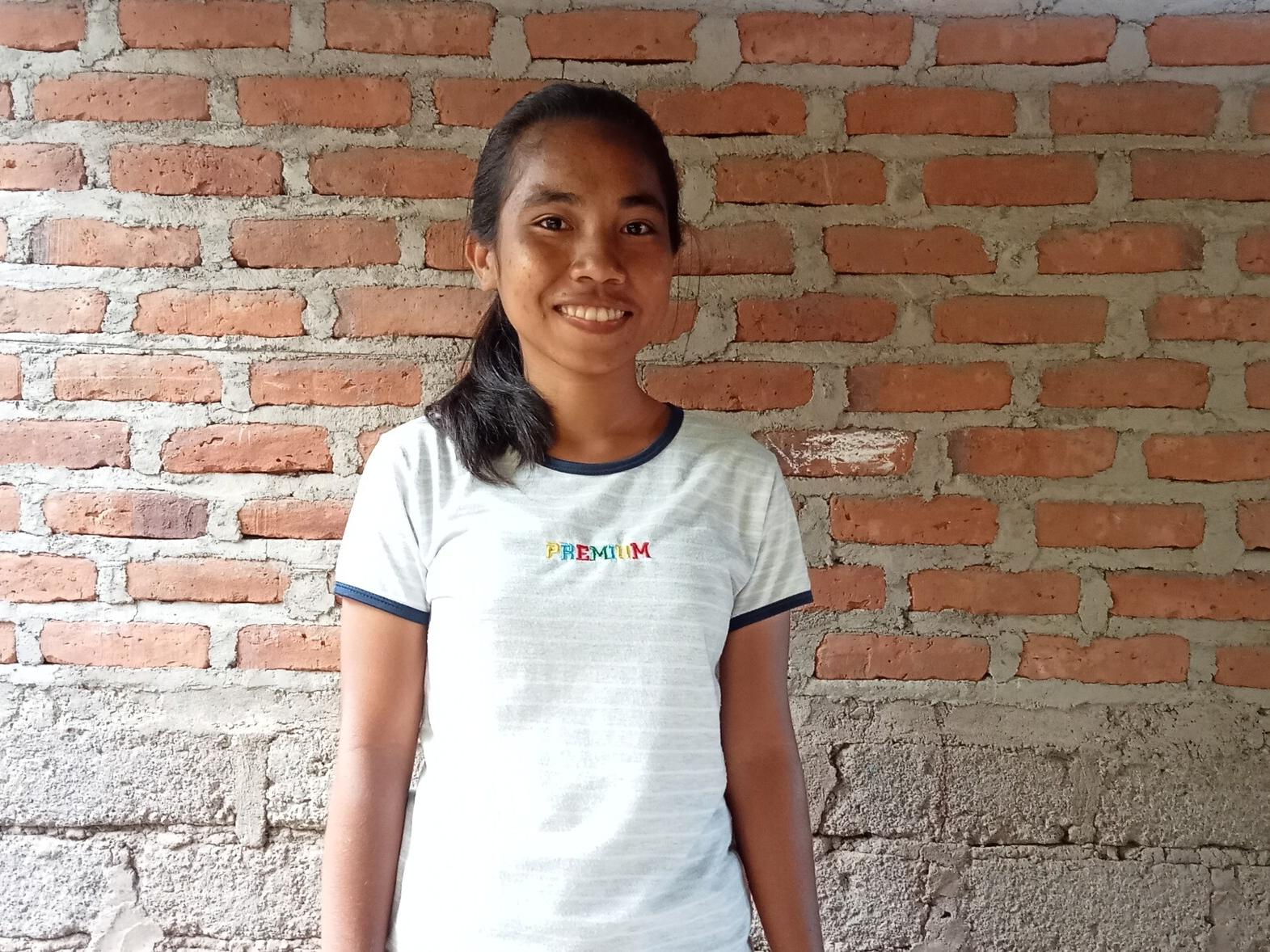 Margareta, 17, standing in front of a brick wall in Indonesia smiling at the camera