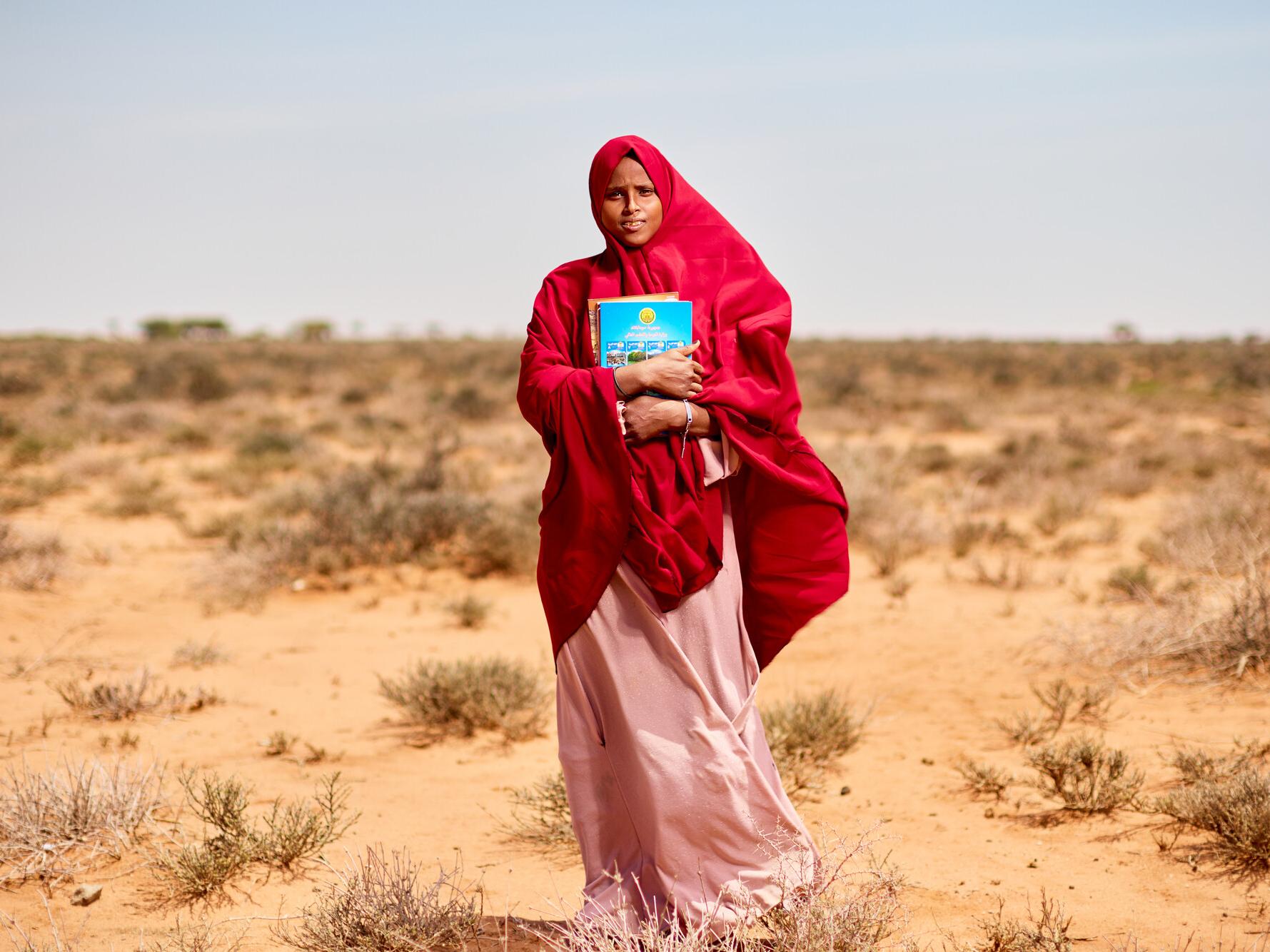 Hibbaq, 18, standing in the bush holding her school books in Somalia.
