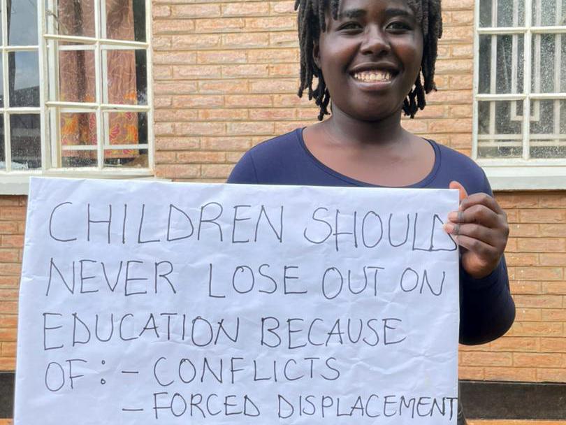 Angela, 24, from Malawi holding a sign that reads: "Children should never lose out on education because of conflict or forced displacement"