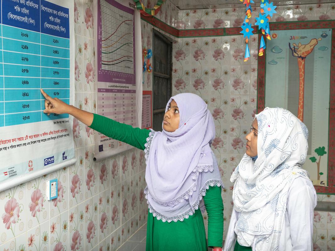 Shahnaz and Sumaya in adolescent corner, pointing at wall chart