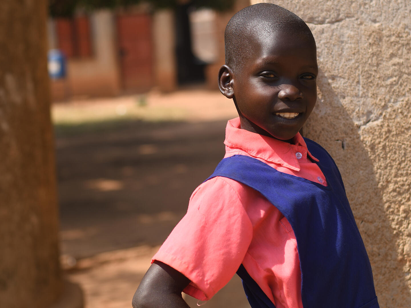 Immaculate, 10, standing outside her school in Uganda smiling at the camera