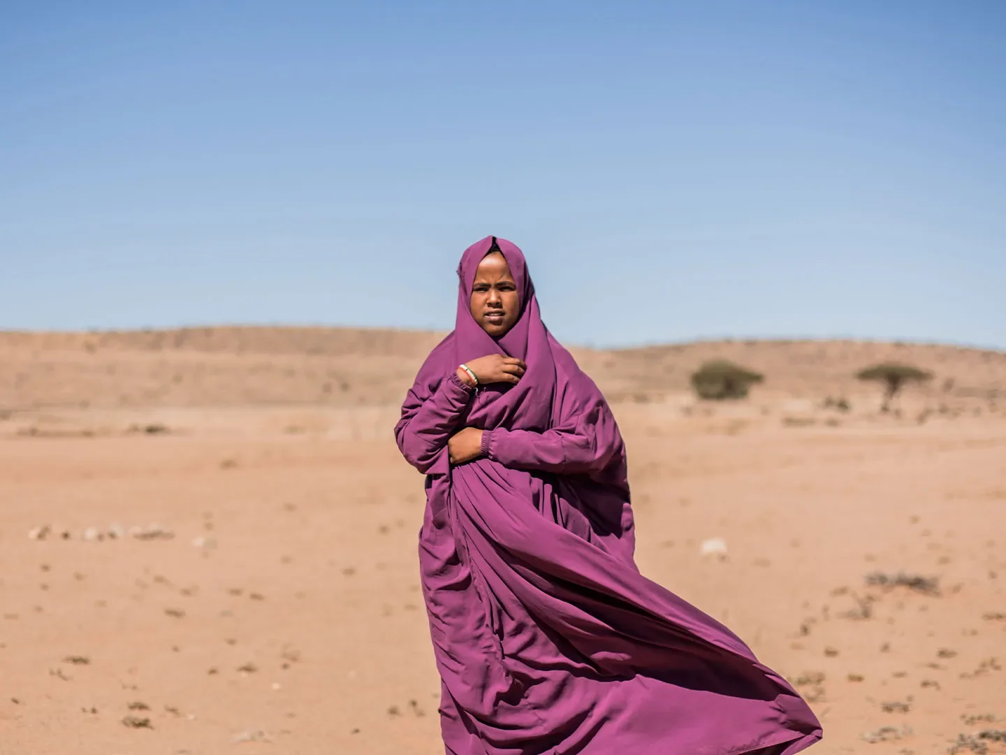 Hamda standing outside in sandy landscape wearing purple robes/headscarf