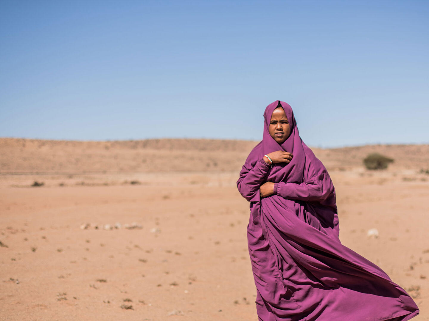 Hamda standing outside in sandy landscape wearing purple robes/headscarf