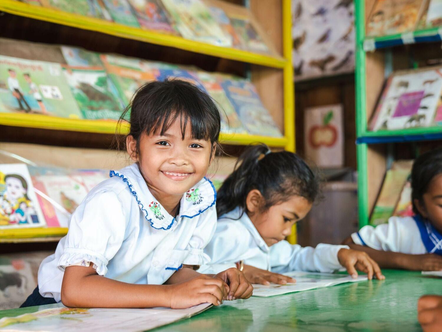 Vorn, 7, reads a book in the library at a primary school built by Plan International in Cambodia