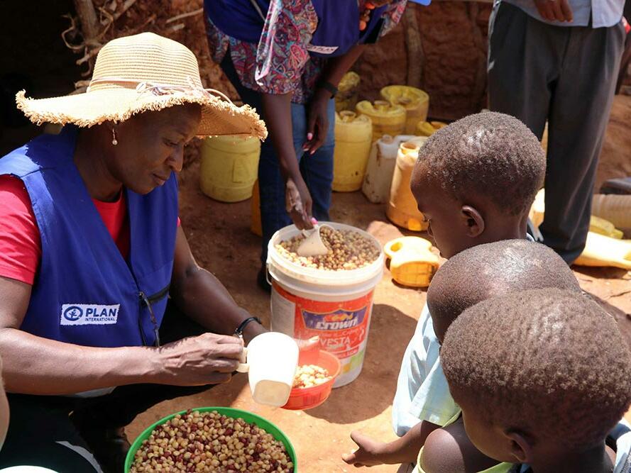 A Plan International staff member distributes school meals to childen in Kenya