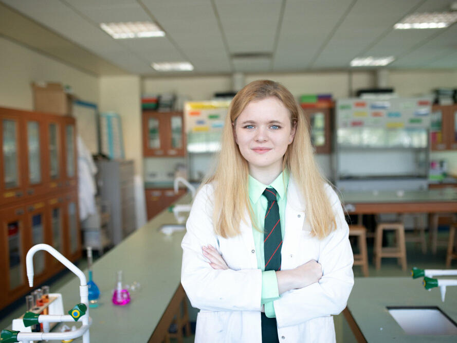 Rachel, 15, standing with her arms crossed in a laboratory class room at her school