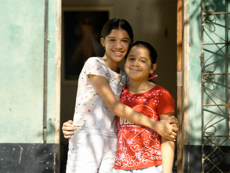 Alana hugging her younger sister in front of sunlit house