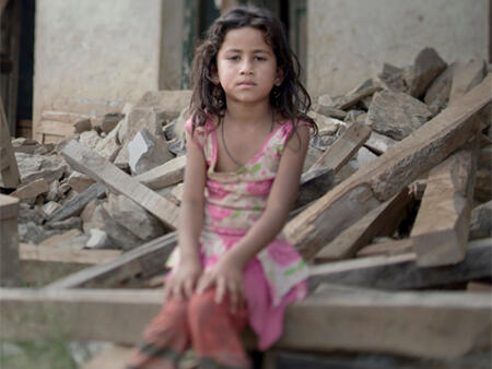 A young girl sitting amongst the ruins of a building after an emergency