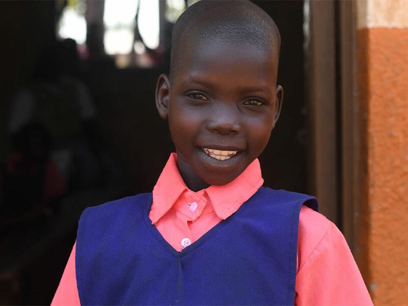 Young girl smiling at camera in pink shirt and blue vest outside school