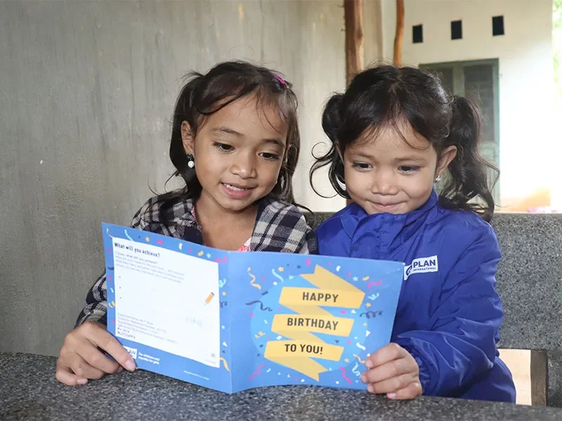 Two young girls happily reading a birthday card from a Plan International sponsor