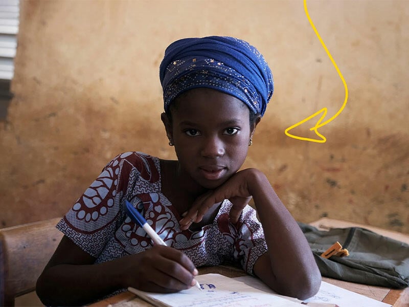 Girl writing at desk at school looking at camera