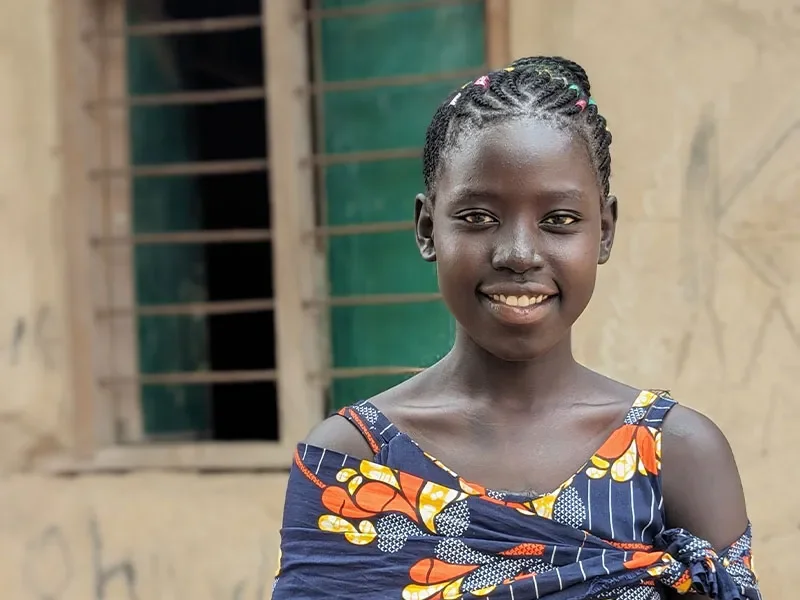 Eighteen year old girl standing in front of building smiling at camera.