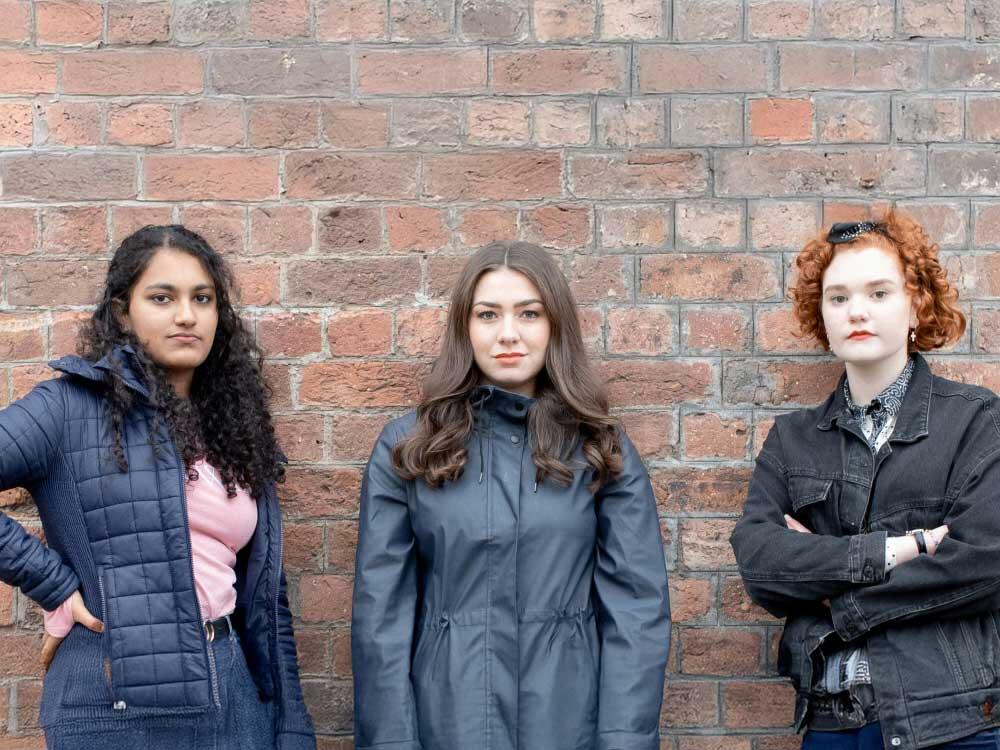 Three young female campaigners standing in front of brick wall