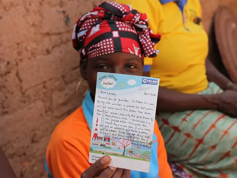 Larissa sat with family and holding letter from sponsor up to camera