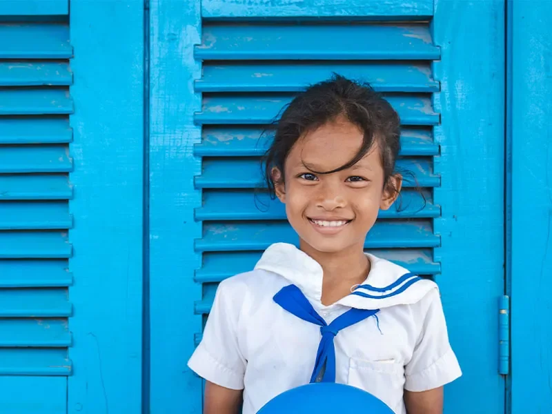 Phen standing in front of bright blue door in school uniform smiling at camera.