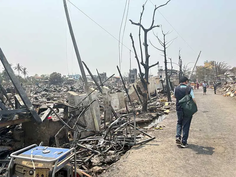 Plan International staff member walking alongside debris of buildings toppled by Myanmar earthquake.