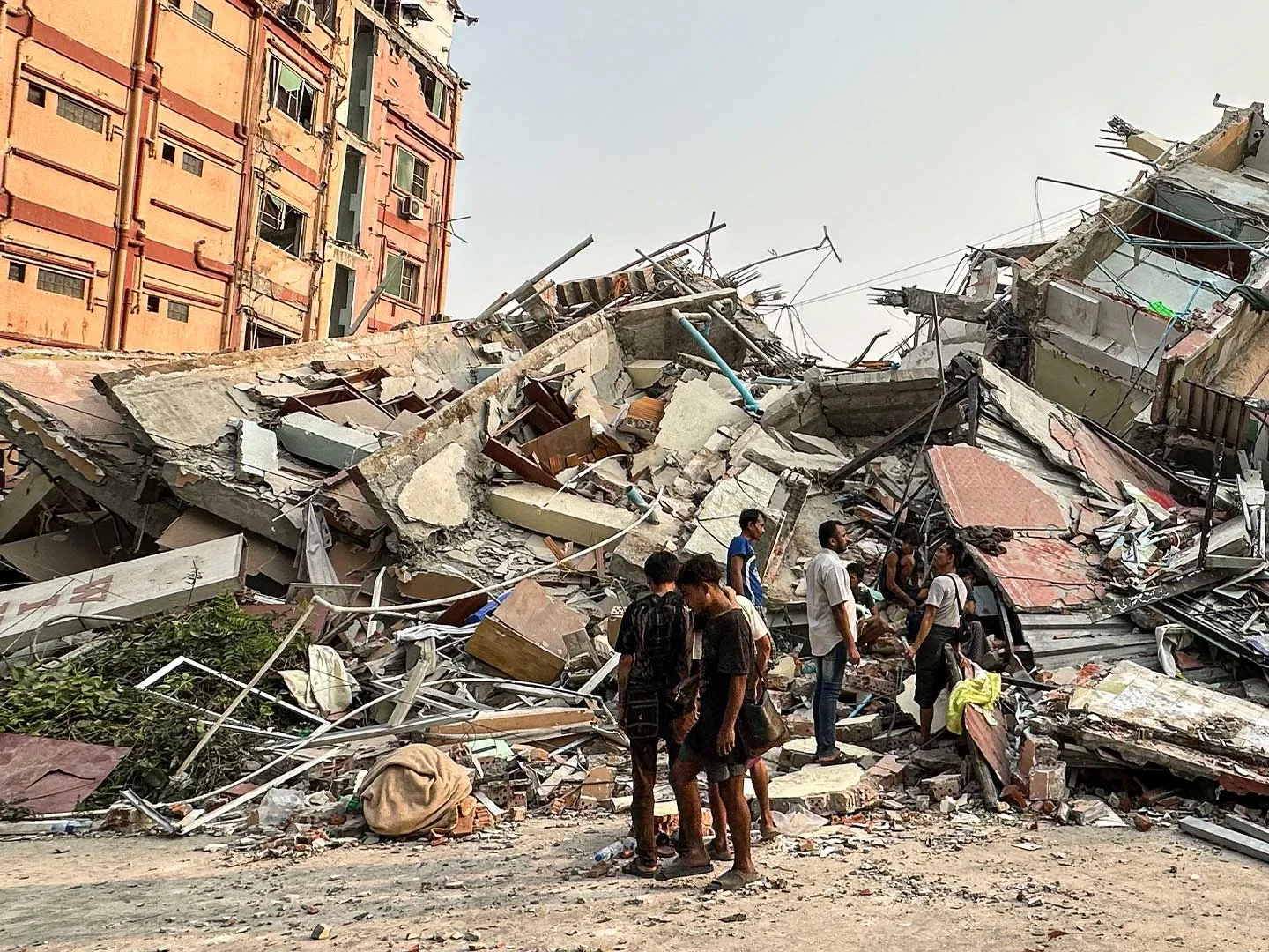 Children and adults standing among collapsed buildings and rubble following Myanmar earthquake.