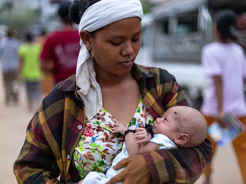 Thida standing with her newborn baby in her arms in the streets of Mandalay.