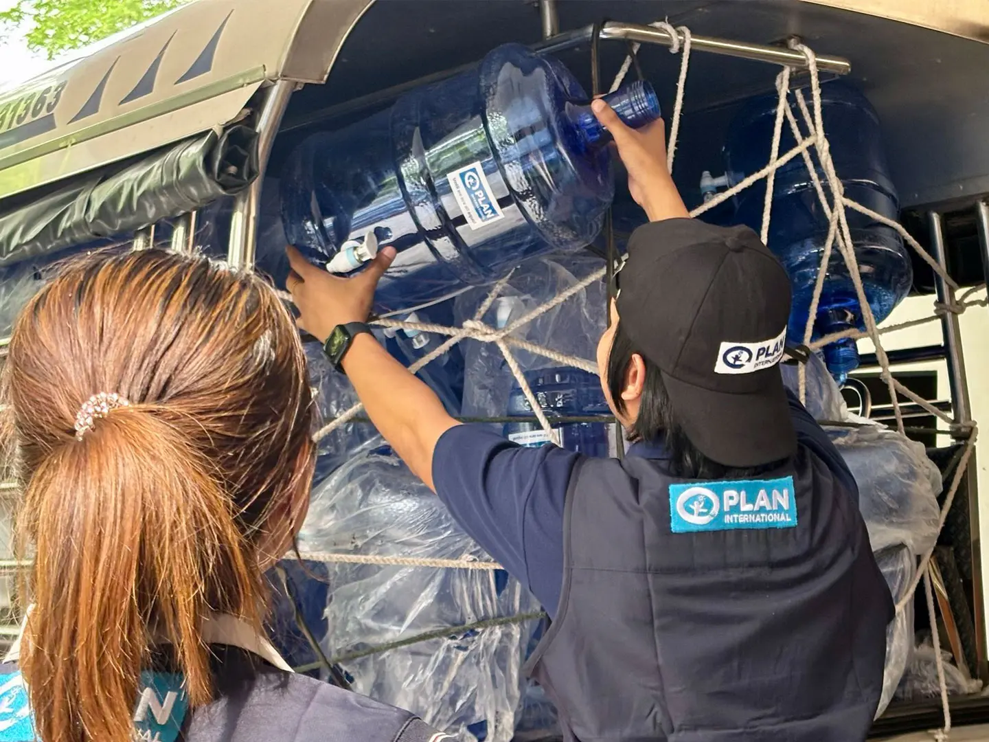 Plan International staff loading large water bottles into the back of a vehicle.