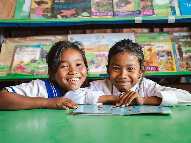 Len Sokha and her school friend sat in school library with open book smiling at camera