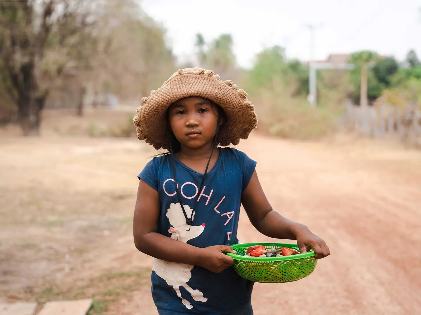 Len Sokha standing outside holding a basket of fruit and a sunhat on