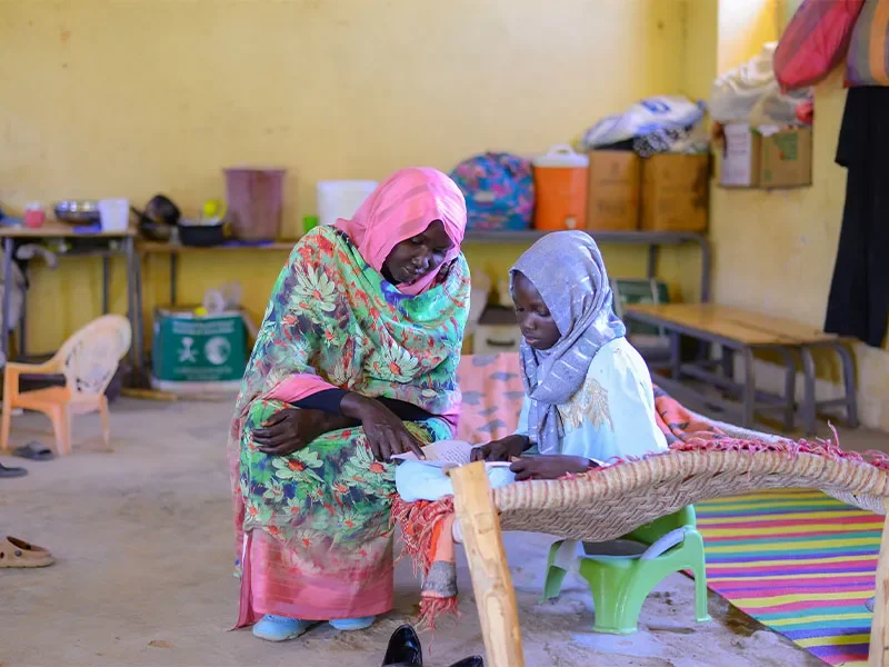 Muna and her mother reading a book in school room. 