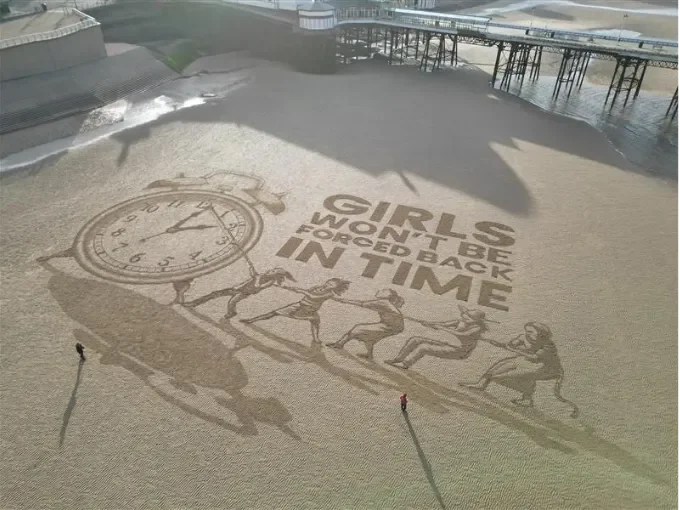 Sand art of a clock face with girls pulling the clock hands and the words 'Girls won' be forced back in time'