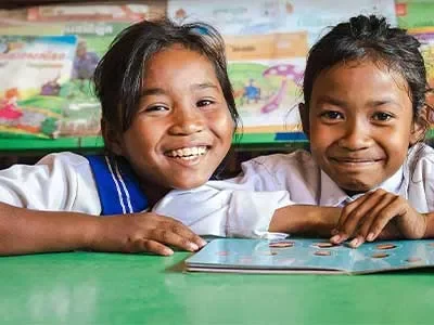 Len Sokha and her school friend sat in school library in Cambodia with open book smiling at camera