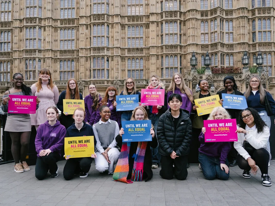 Young people stand outside parliament with placards supporting girls'rights