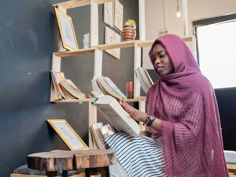 Safa sat down reading in her cafe. There is a shelf of books behind her.