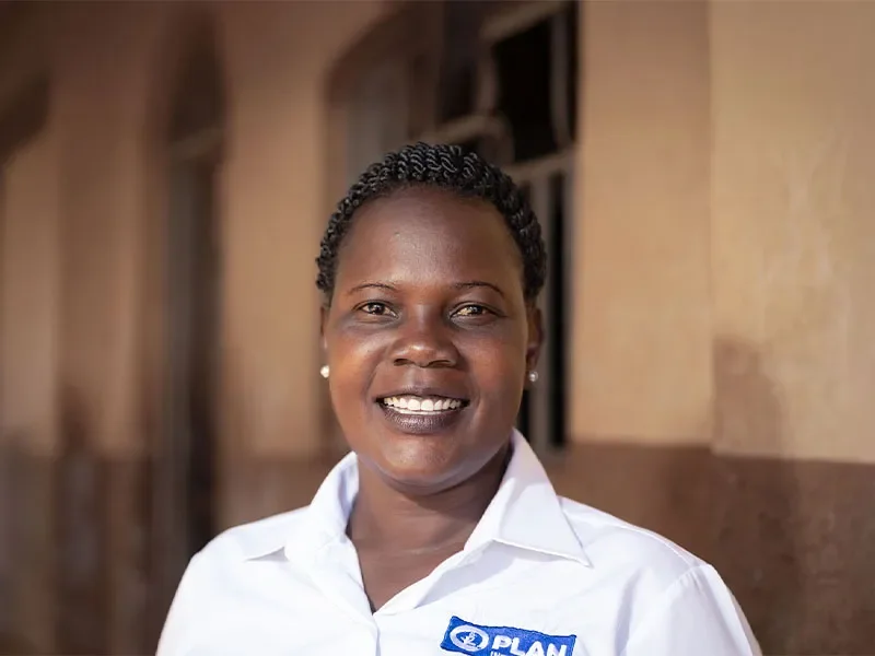 Plan International staff member standing in front of building in Plan International branded polo shirt.