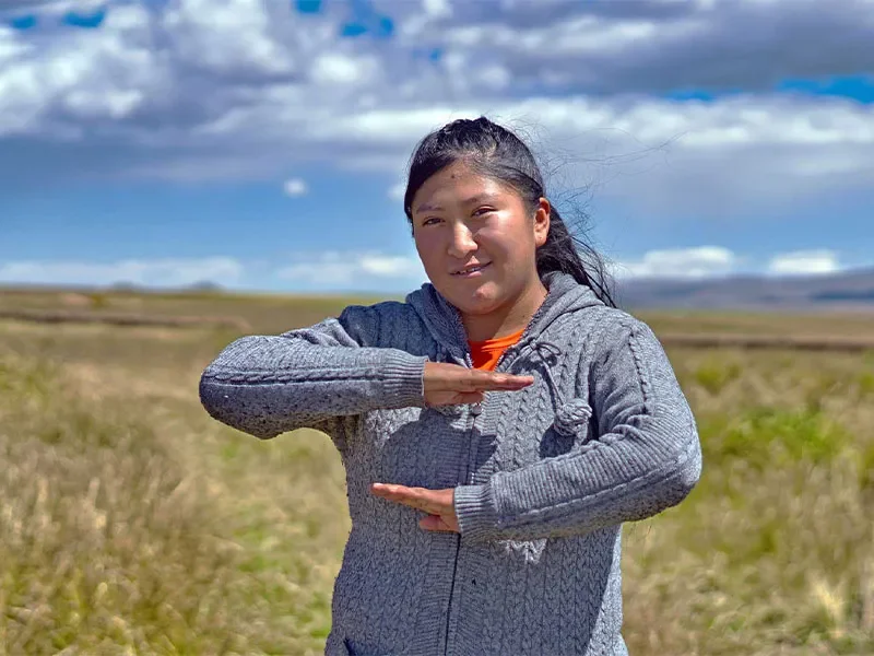 Geovana standing in field with arms out in front of her gesturing no to patriarchy