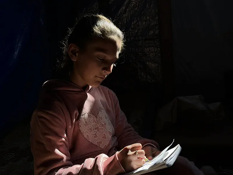 Elin, 11, in Northern Gaza, sits in a tent. She is drawing.