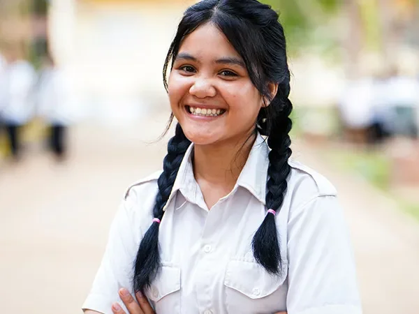 Sopheak, 15, from Cambodia, stands with folded arms. She is wearing a white shirt and smiling at the camera.