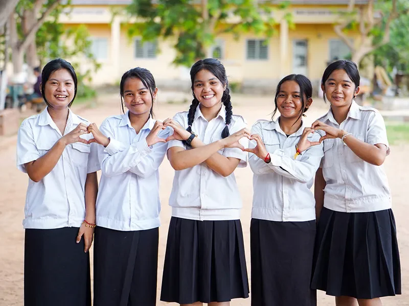 Sopheak, 15, from Cambodia, with her friends. They are making heart shapes with their hands.