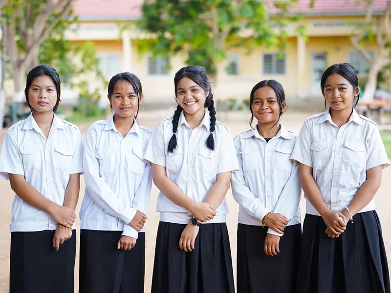 Sopheak, aged 15, stands in the centre of a group of friends. They are wearing white shirts and smiling at the camera.