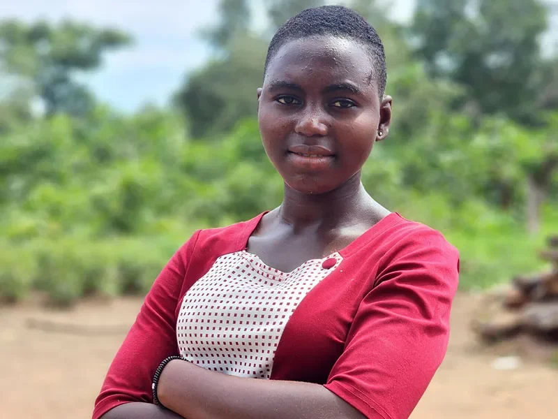 Dorcas, 16, from Togo, stands wearing a red dress. She has her arms folded.