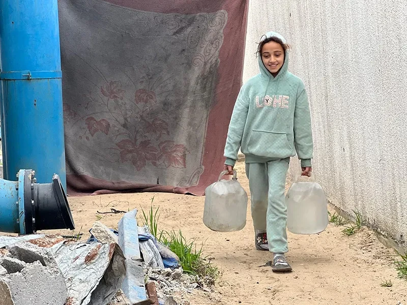 Farah, 11, from Gaza, carries two jugs of water to her family's tent.