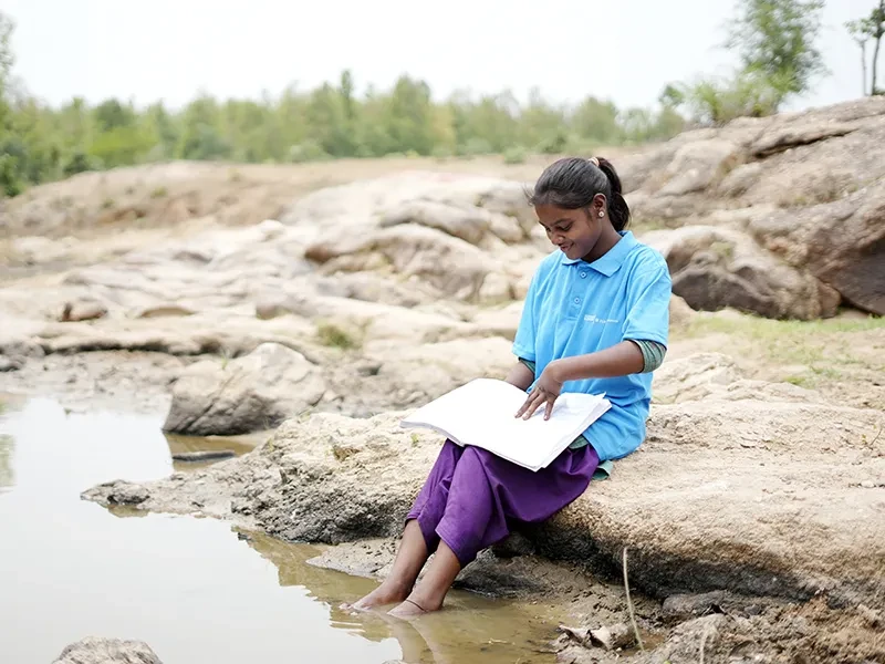 Rajni, from India, sits on the side of a river with a book.