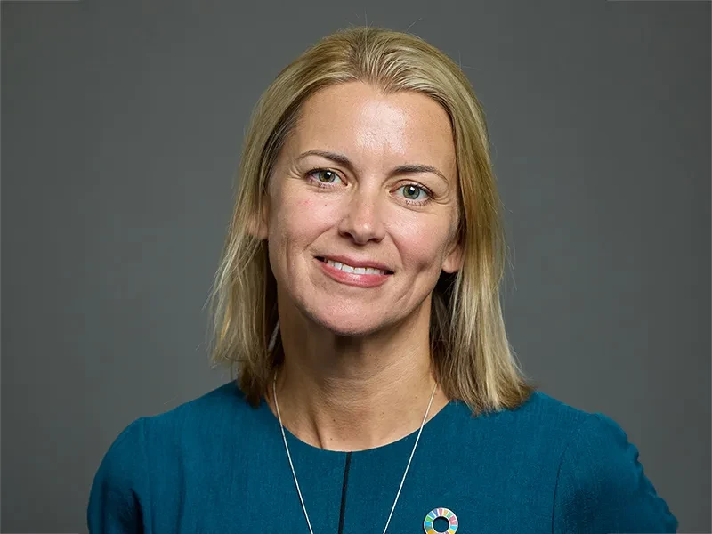 Baroness Liz Sugg looks at the camera. She is wearing a blue top and a necklace.