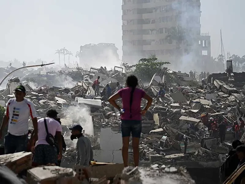 People walking through rubble of destroyed buildings in Venezuela with focus on back of girl standing and looking at it.